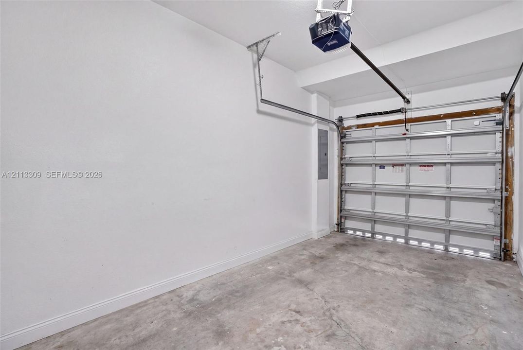 Garage interior featuring white finished walls, concrete flooring, a paneled overhead door, and an integrated automatic garage door opener