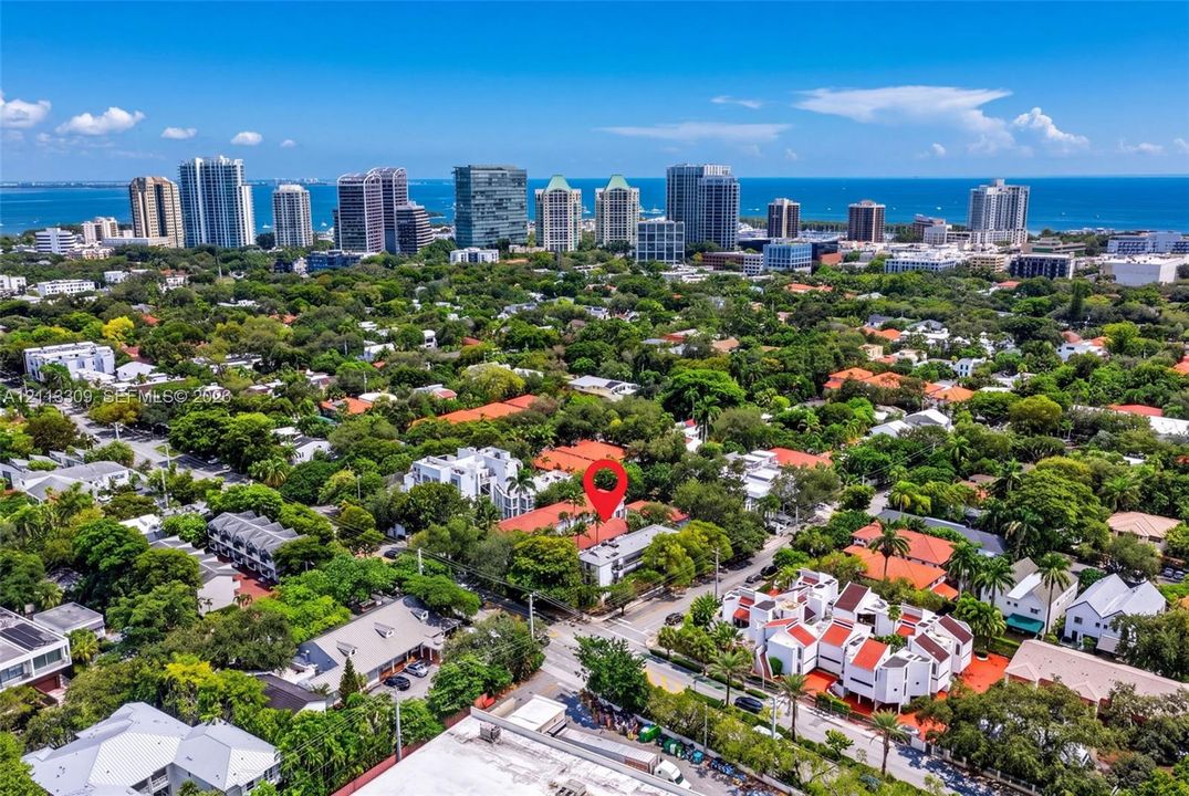 Aerial perspective highlighting a multi-unit residential structure featuring white exterior masonry and terracotta-style roof tiles, situated within a dense canopy of mature trees with proximity to a coastal skyline