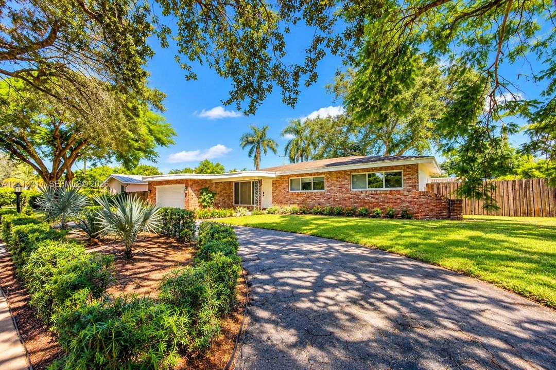Ranch-style exterior featuring a multi-tonal brick façade, an attached single-car garage, an expansive manicured lawn, established landscaping, and a curved driveway