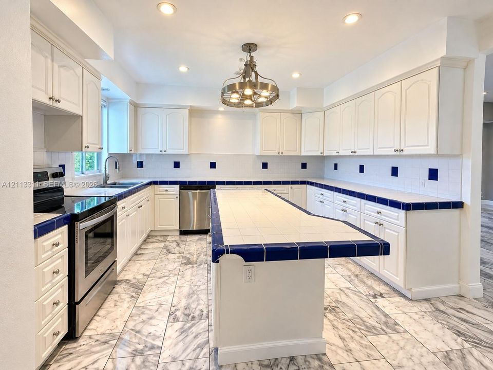 Kitchen featuring white cabinetry, an expansive central island, tile countertops with contrasting trim, stainless steel appliances, and stone-finish flooring