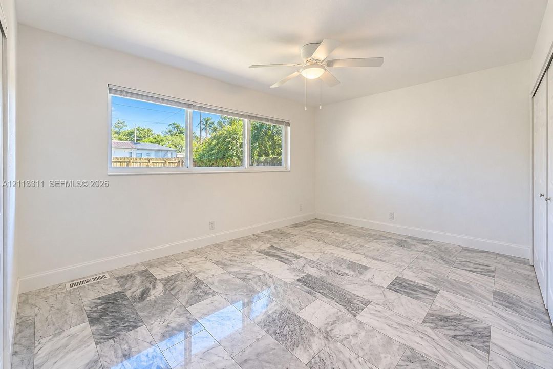 Room featuring polished stone tile flooring, a horizontal multi-pane window, and a ceiling-mounted light fixture with a central fan