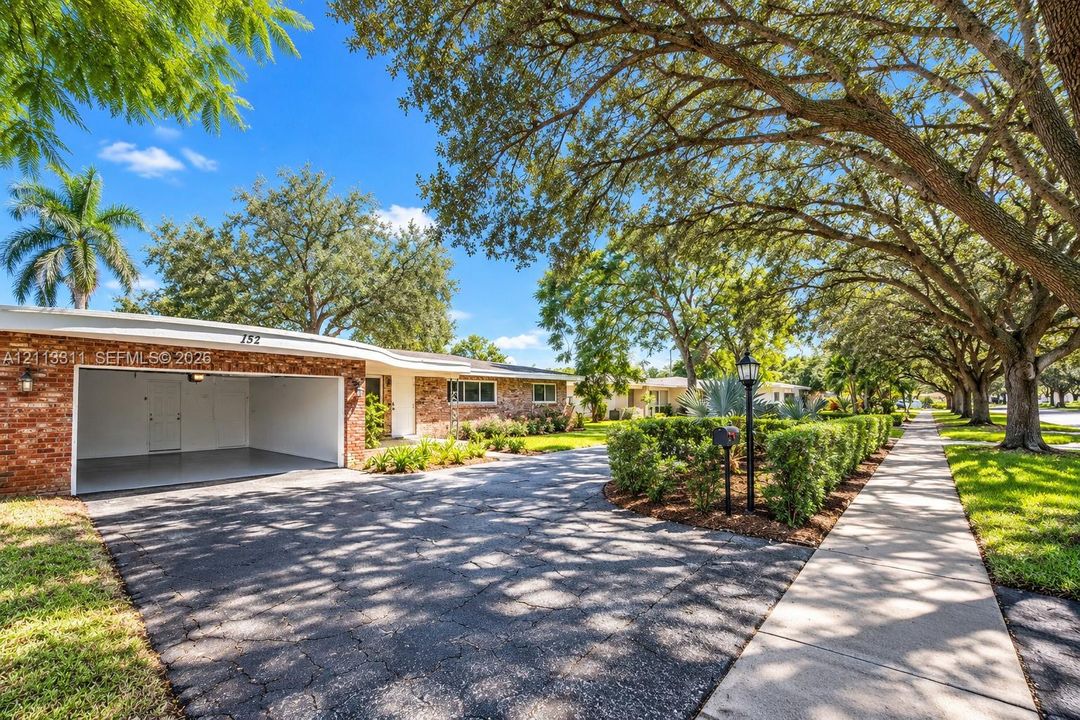 Exterior featuring a brick facade, integrated garage, paved driveway, and mature landscaping