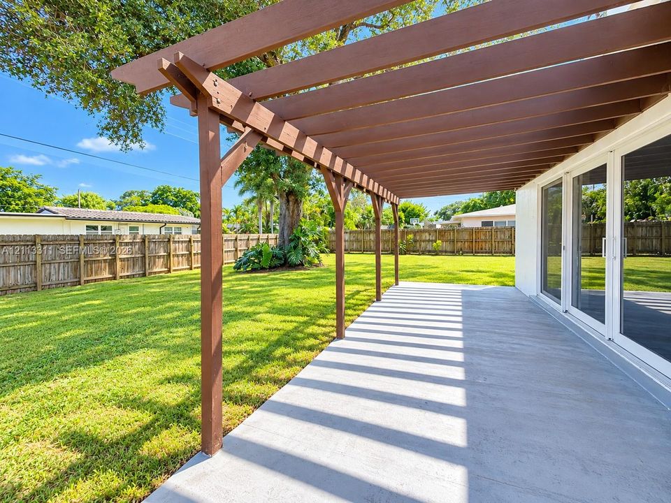 Covered patio featuring a timber-frame pergola, concrete flooring, sliding glass door entry, and a fenced backyard with mature landscaping