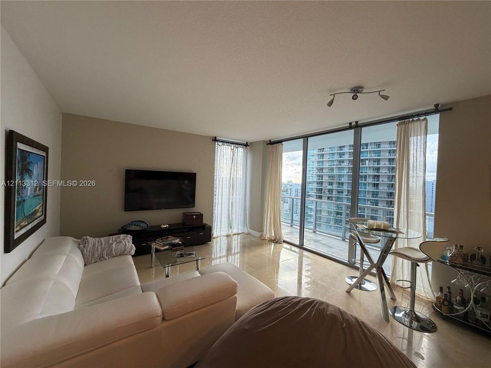 Floor-to-ceiling glass wall, polished tile flooring, integrated balcony access, and track lighting