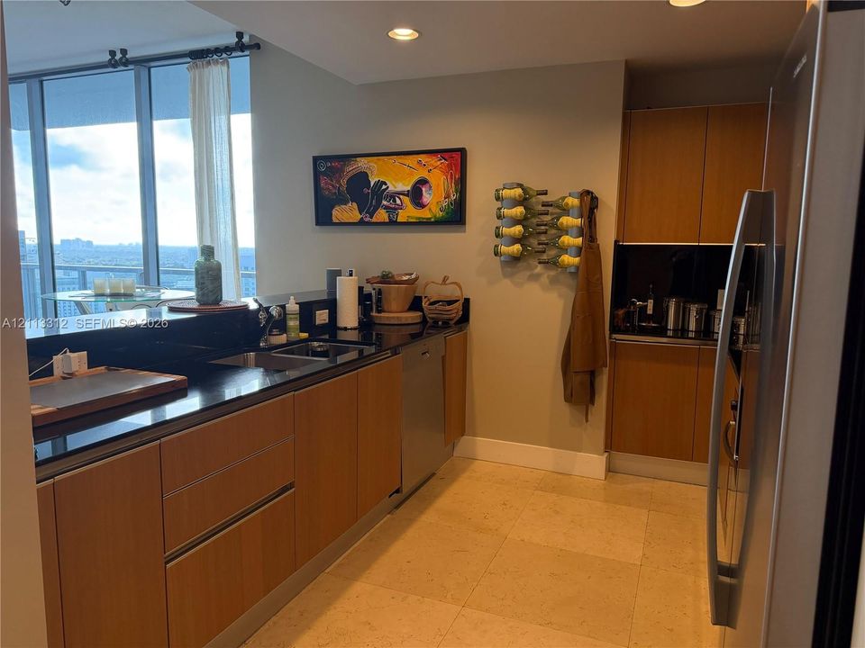 Kitchen featuring flat-panel wood cabinetry, black solid-surface countertops, recessed ceiling lighting, full-height windows, and light-toned stone flooring