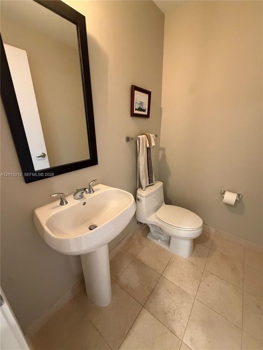 White pedestal sink with chrome faucet, neutral tile flooring, and wall-mounted mirror with a dark frame