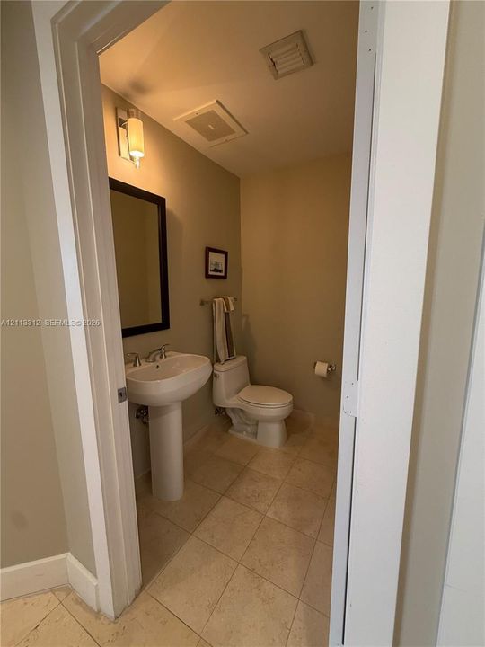 Powder room featuring a porcelain pedestal sink, stone-finish floor tiling, wall-mounted vanity lighting, and a framed mirror