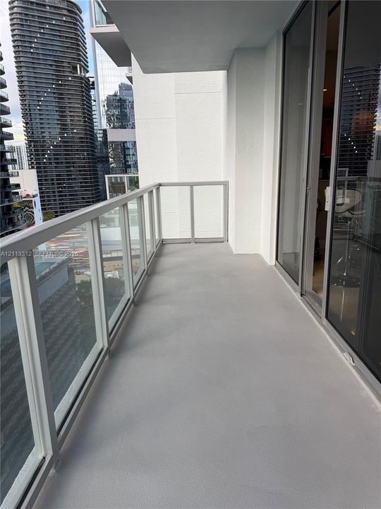 Private balcony featuring neutral concrete flooring and a glass-paneled railing with a metal frame, accessible via floor-to-ceiling sliding glass doors