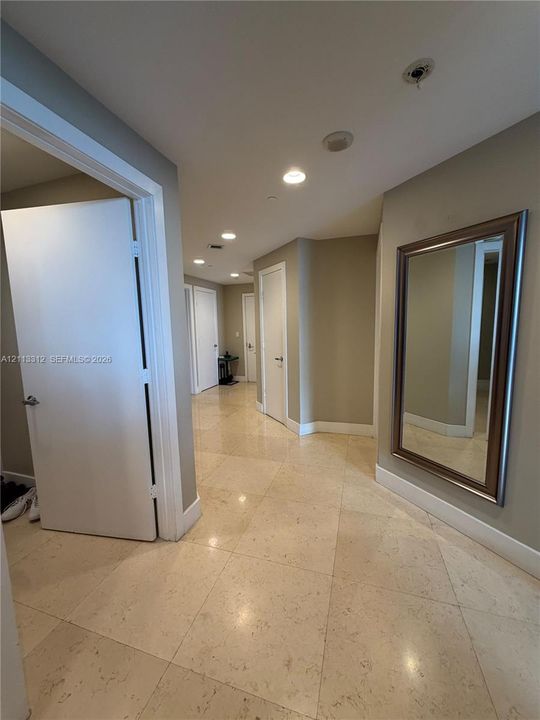 Interior hallway featuring large-format stone tile flooring, recessed ceiling lighting, and solid-core interior doors with metallic hardware