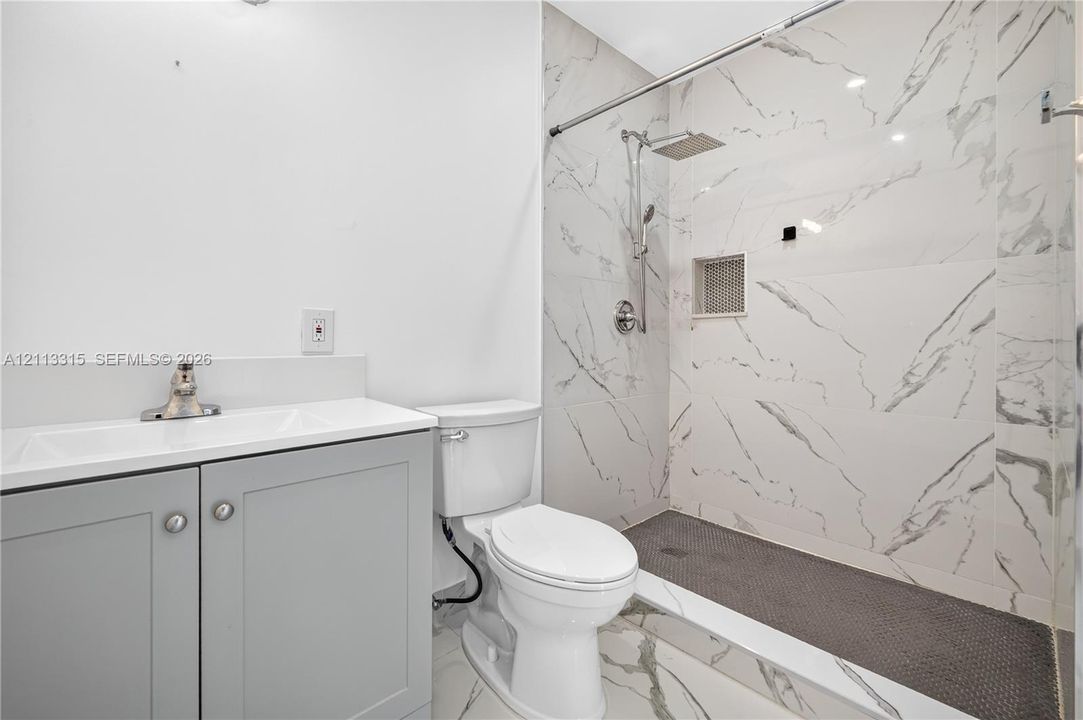 Bathroom featuring a grey vanity with a white integrated sink, walk-in shower with floor-to-ceiling stone-look tile, rain-style shower head, and built-in recessed wall niche