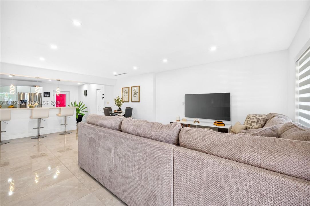 Open-concept interior featuring large-format polished tile flooring, recessed ceiling lighting, a breakfast bar with stone-finish surfacing, and horizontal window blinds