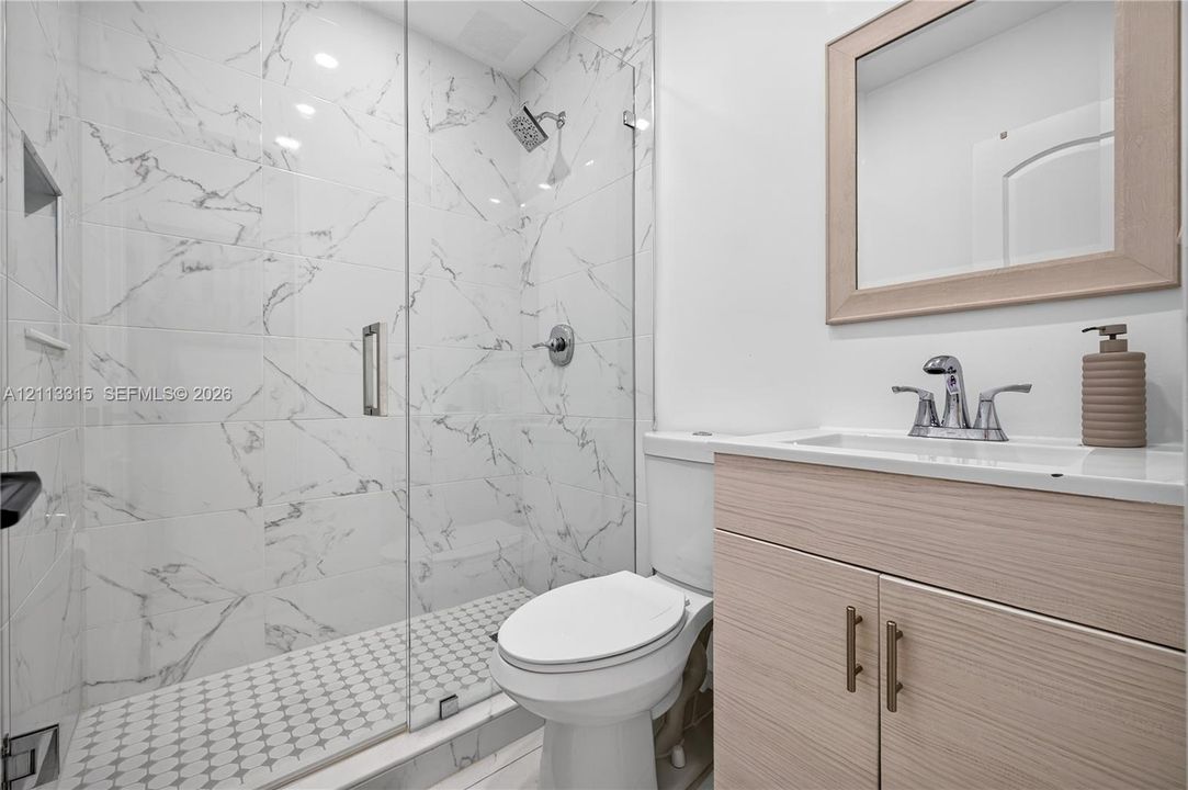 Walk-in shower featuring large-format stone-patterned tile walls, a frameless glass door, and a geometric mosaic tile floor