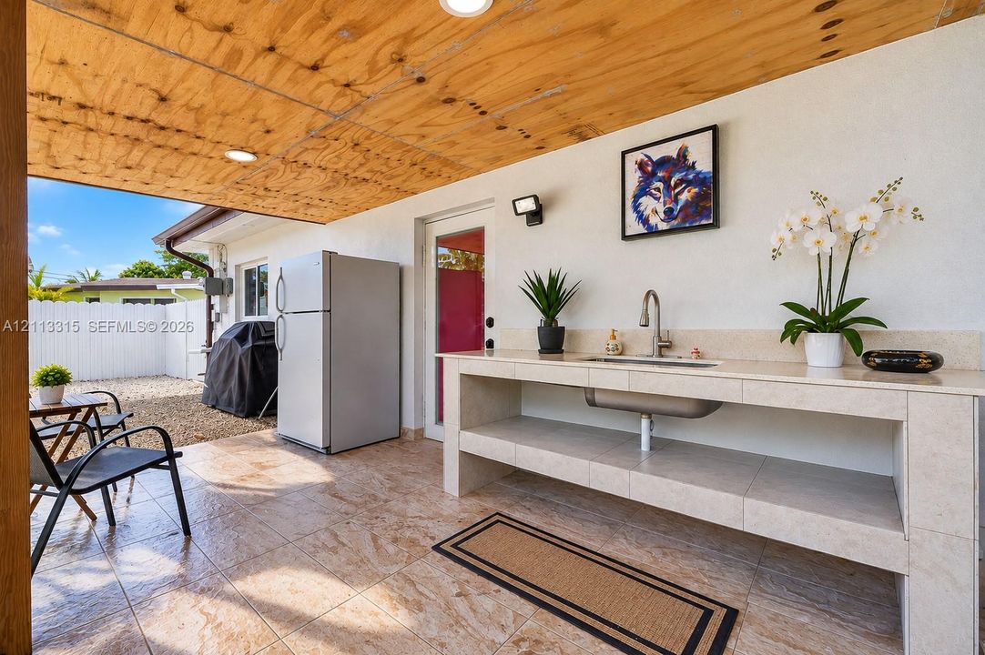 Covered patio featuring a wood-paneled ceiling, tiled flooring, built-in outdoor wet bar with a stone-finish countertop, and recessed lighting