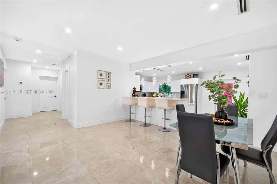 Large-format tile flooring, recessed ceiling lighting, and a breakfast bar with stone-finish countertops