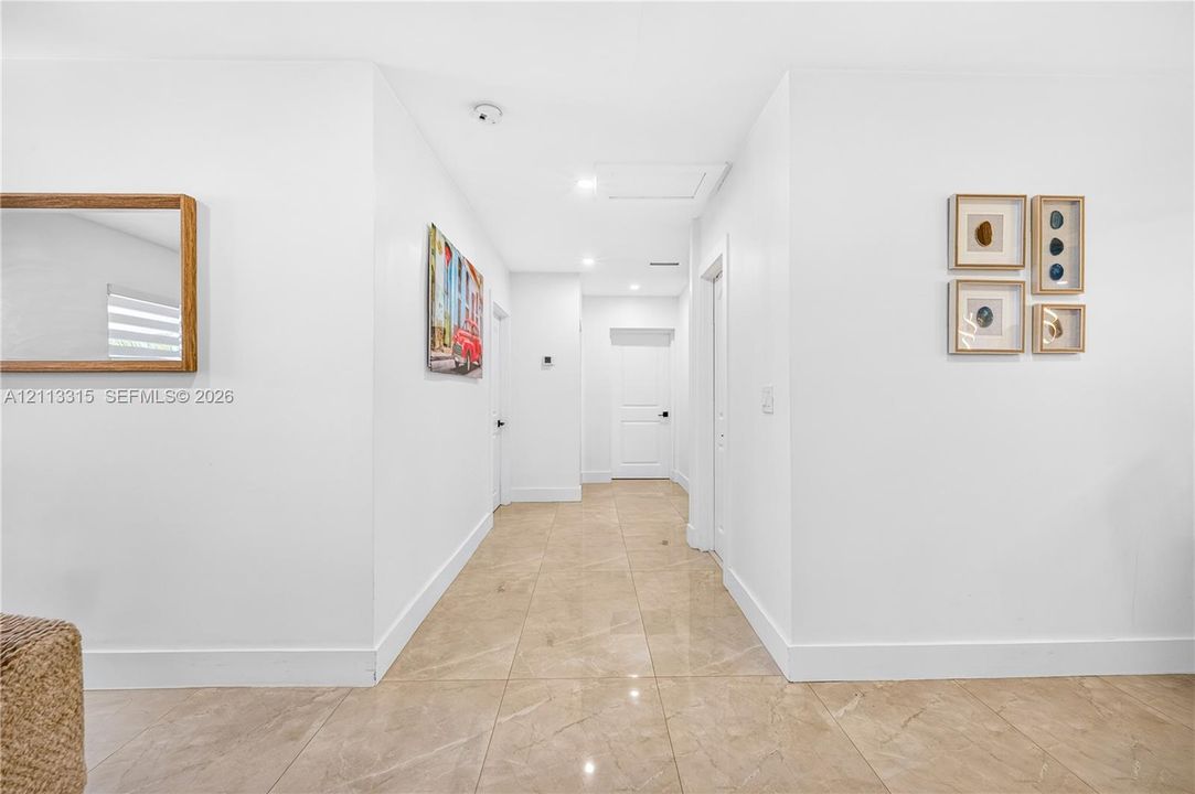 Neutral-toned polished tile flooring, crisp white walls, recessed ceiling lighting, and solid-core interior doors with matte black hardware