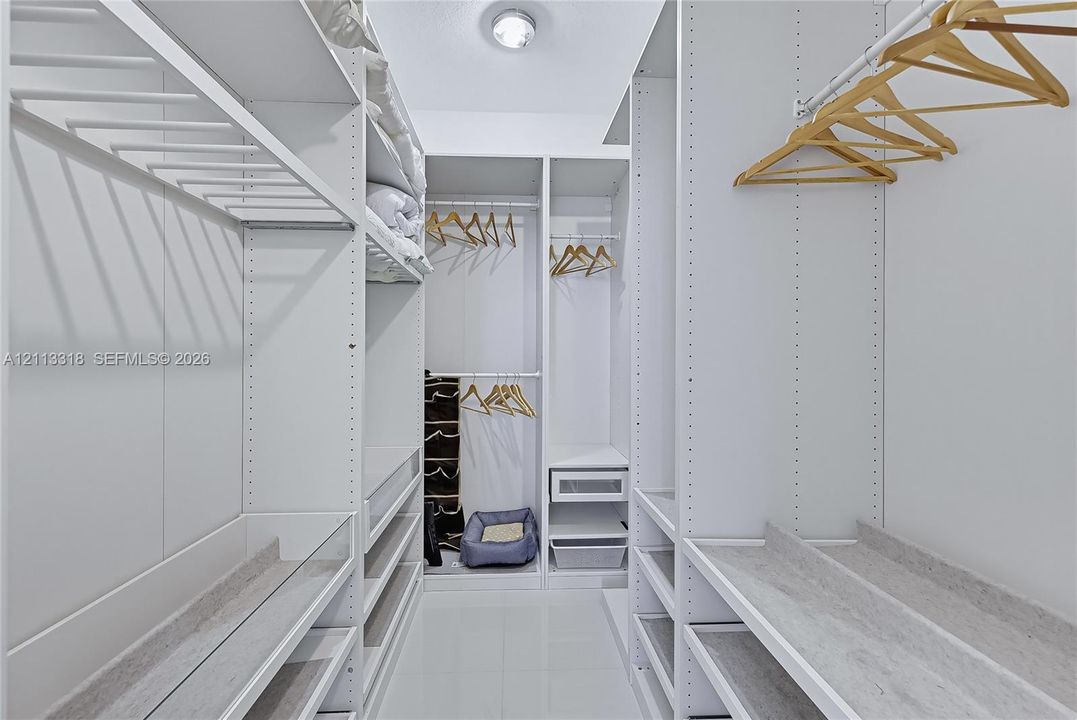 Walk-in closet featuring floor-to-ceiling white built-in shelving, adjustable storage racks, integrated hanging rods, and glossy tile flooring