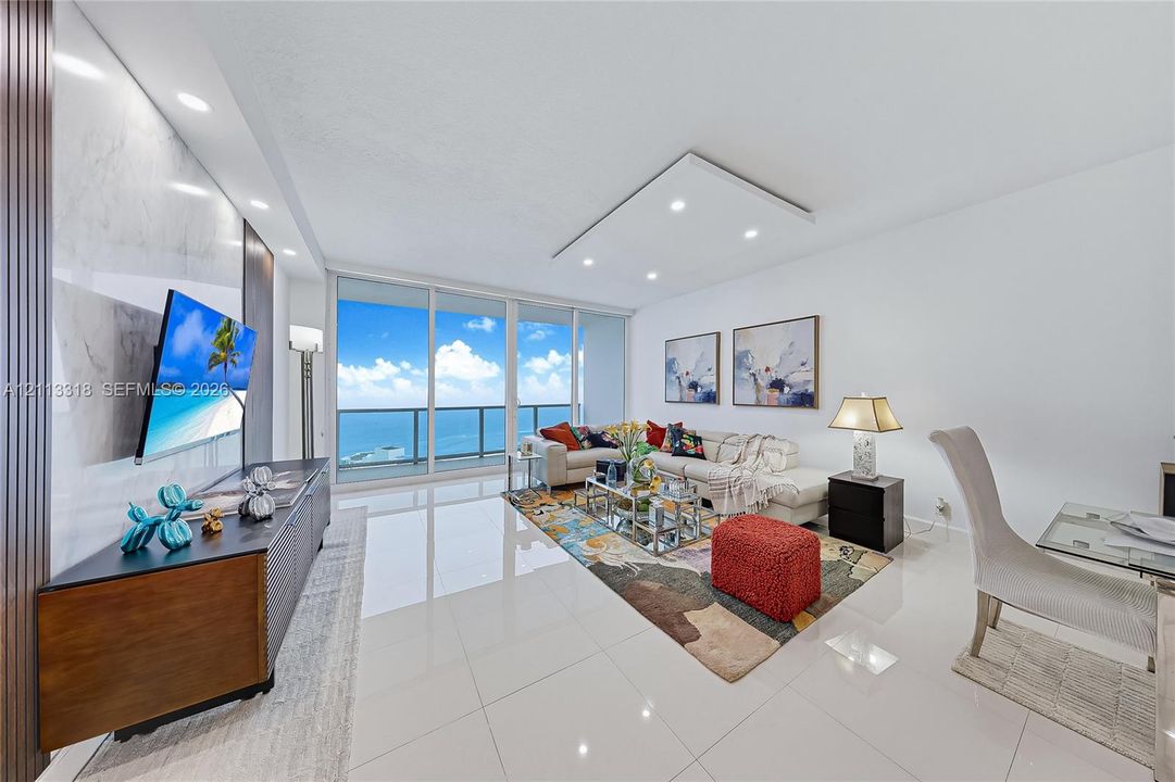 Living area featuring floor-to-ceiling glass sliding doors, polished tile flooring, recessed ceiling lighting, and a floor-to-ceiling stone-finish accent wall