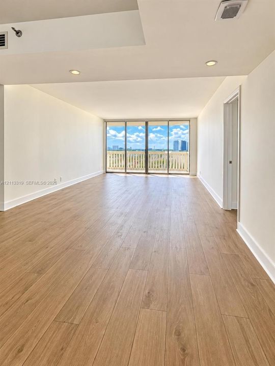Open interior featuring wood-finish flooring, recessed lighting, and floor-to-ceiling glass sliding doors opening to an exterior balcony