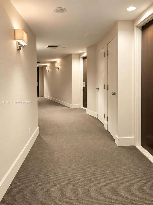 Interior corridor featuring neutral wall-to-wall carpeting, recessed ceiling lighting, wall-mounted sconces, and solid-core interior doors