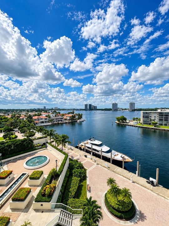 Waterfront terrace featuring a decorative fountain, linear water feature, paver hardscaping, mature landscaping, and private bulkhead dockage