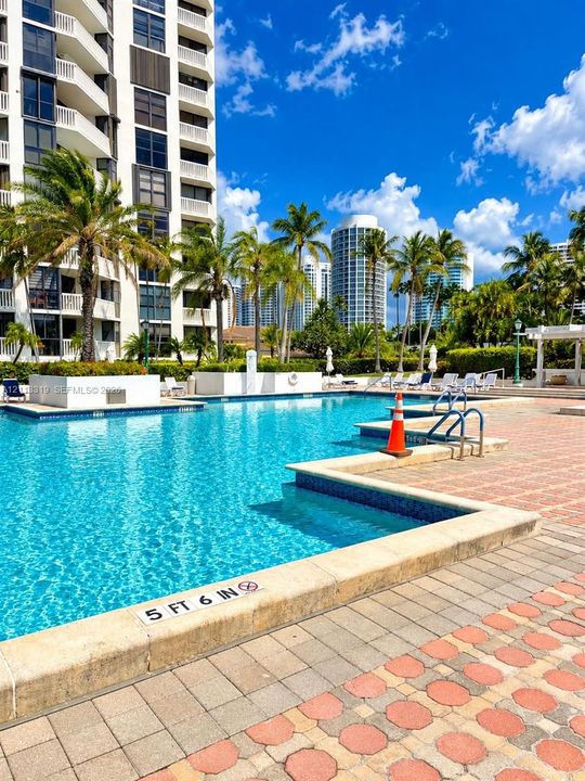 In-ground swimming pool featuring a tiled perimeter, stone paver decking, built-in planters, and palm tree landscaping