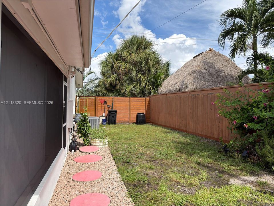 Private backyard featuring a horizontal wood-slat perimeter fence, gravel pathway with circular concrete pavers, and mature palm trees