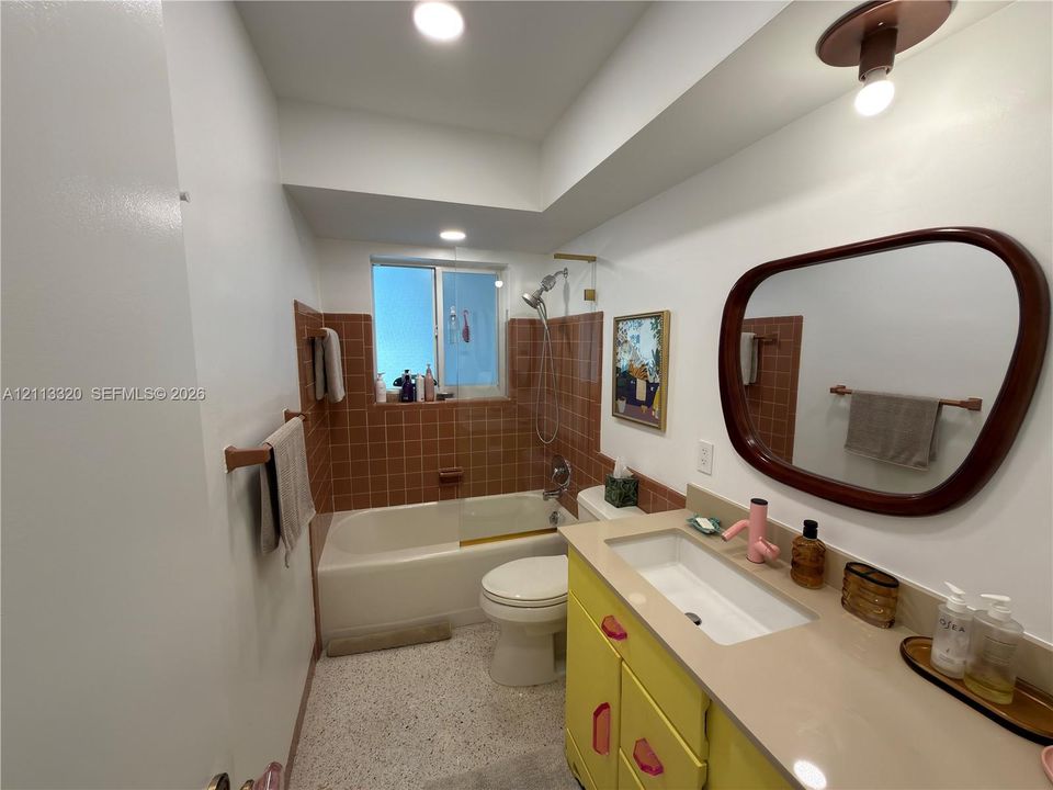 Bathroom featuring a vanity with integrated rectangular sink, solid surface countertop, tiled tub surround, recessed lighting, and terrazzo-style flooring