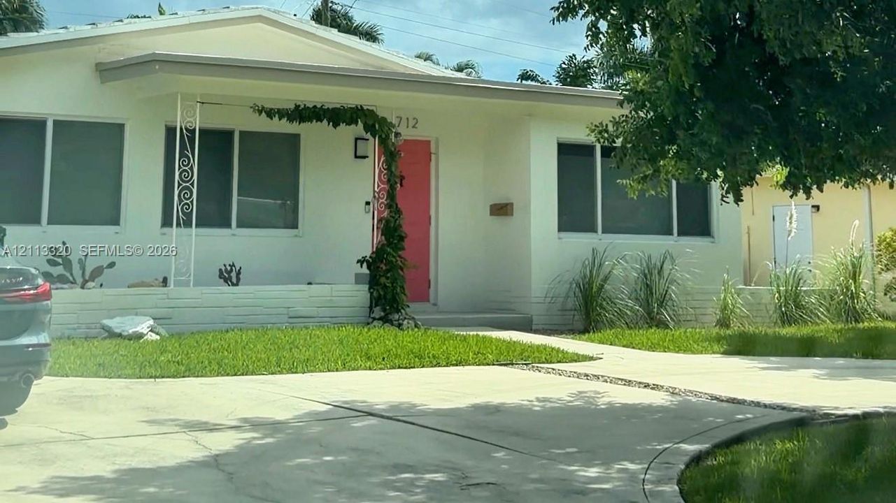 Single-story exterior featuring a light-colored stucco facade, decorative wrought iron porch support, a vibrant entry door, and a concrete driveway