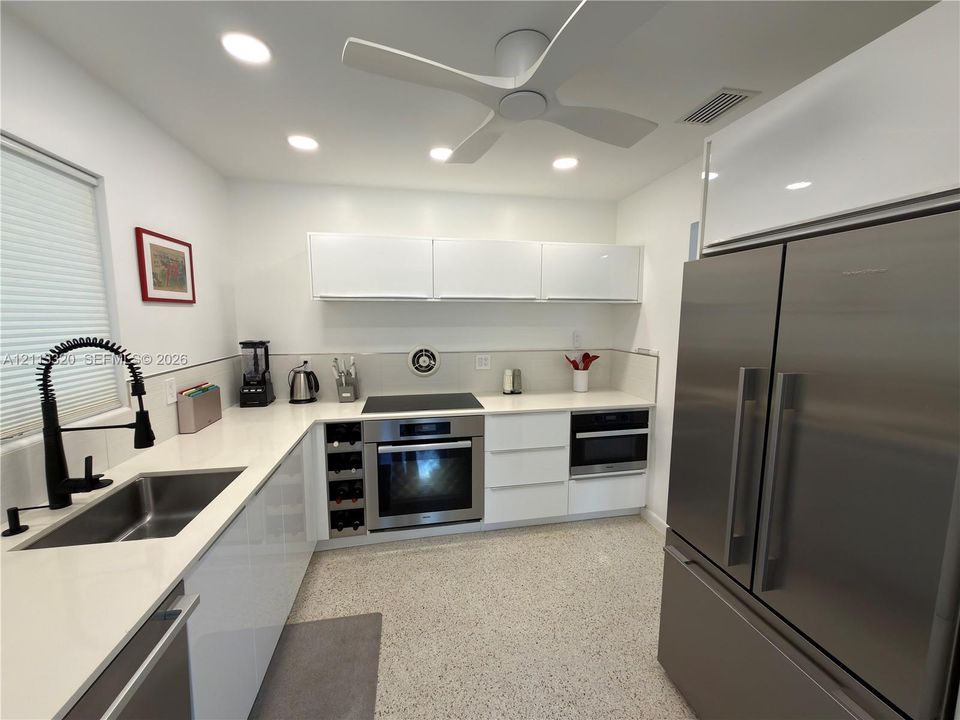 Modern kitchen featuring flat-panel white cabinetry, stone-finish countertops, stainless steel appliances, a built-in wine rack, and terrazzo flooring