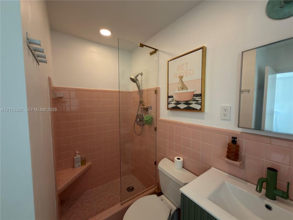 Bathroom featuring a glass shower panel, built-in tiled corner bench, handheld showerhead, wall-mounted vanity with a rectangular basin, and decorative tile wall surrounds