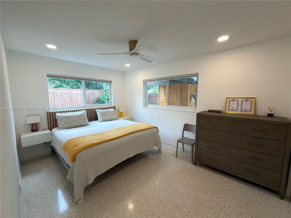 Terrazzo flooring, recessed ceiling lighting, wall-mounted floating bedside tables, and a three-blade ceiling fan