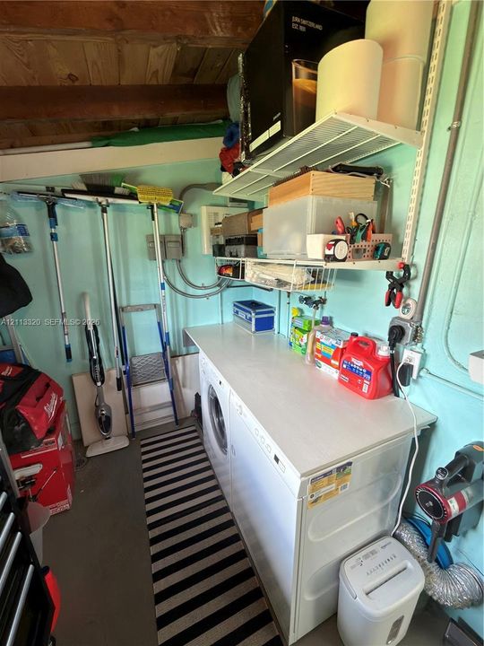 Utility area featuring integrated laundry appliances with a flat work surface, adjustable wire wall shelving, exposed wood ceiling beams, and concrete flooring
