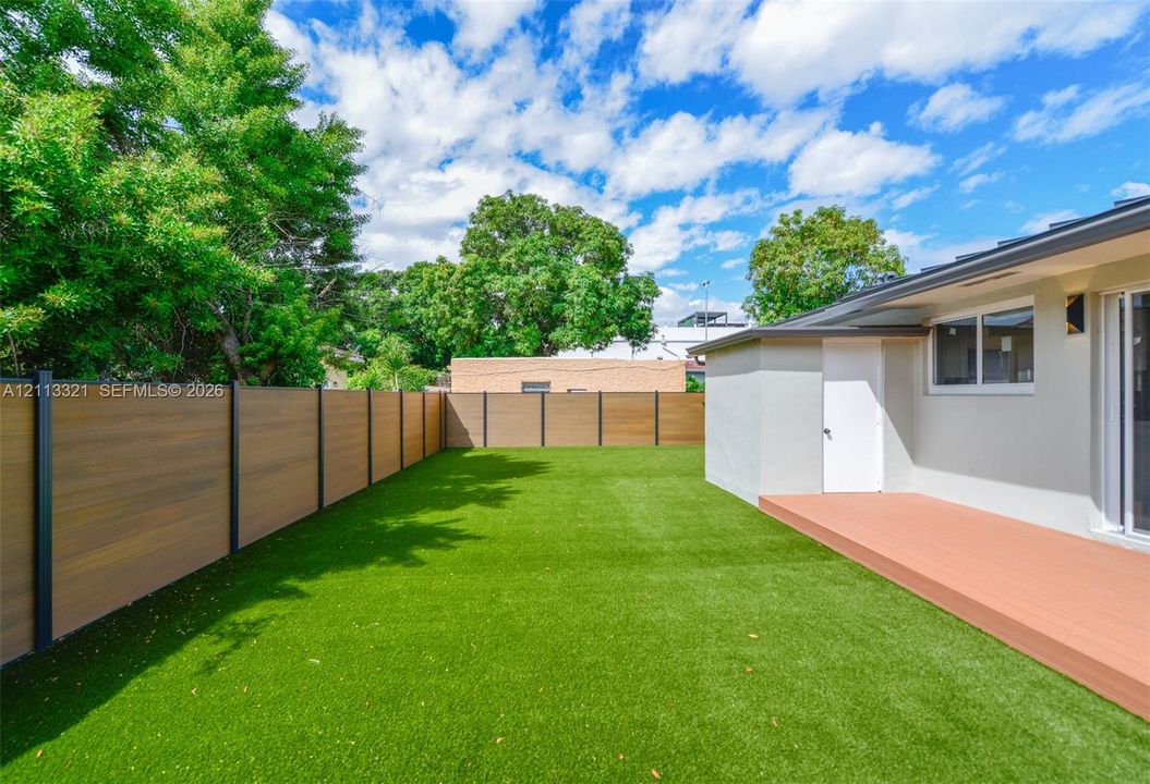 Private backyard featuring synthetic turf, wood-finish privacy fencing, and a built-in exterior deck