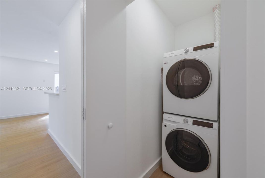 Stacked laundry center featuring white front-load appliances and wood-finish flooring