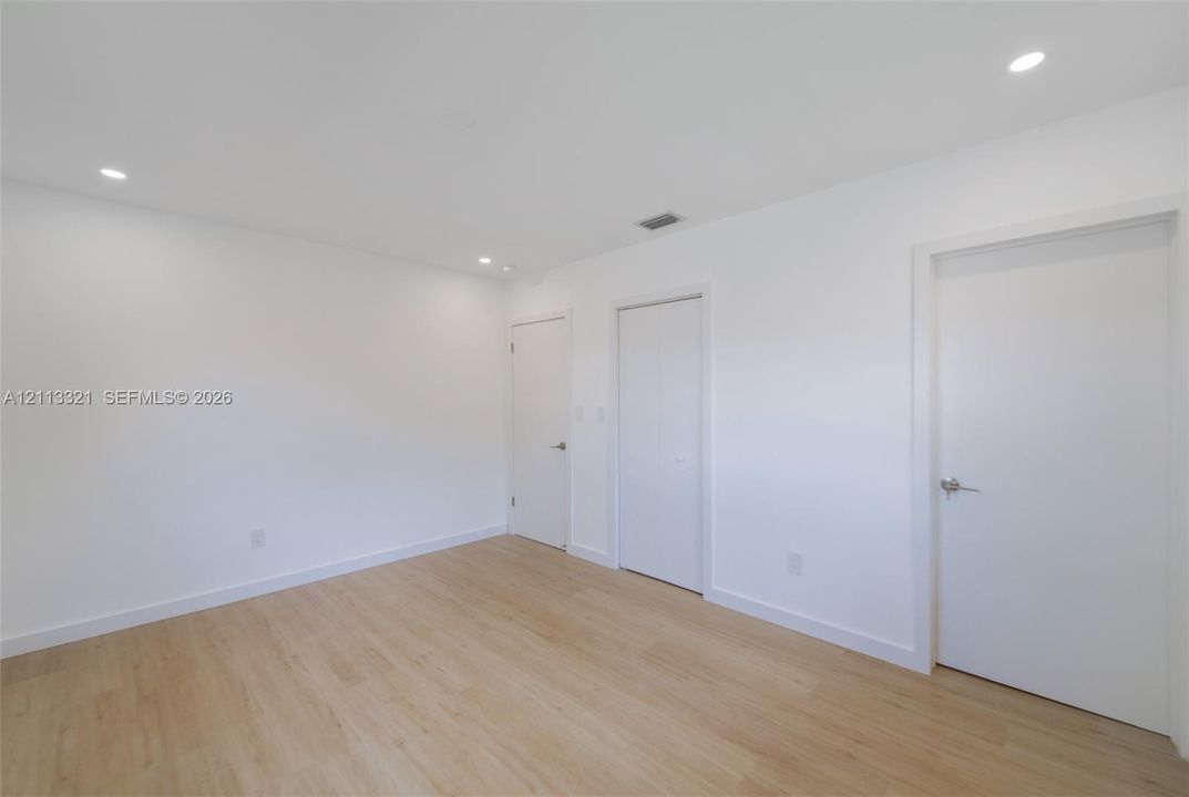 Neutral-toned space featuring wood-finish flooring, recessed lighting, and multiple interior doors with brushed nickel hardware