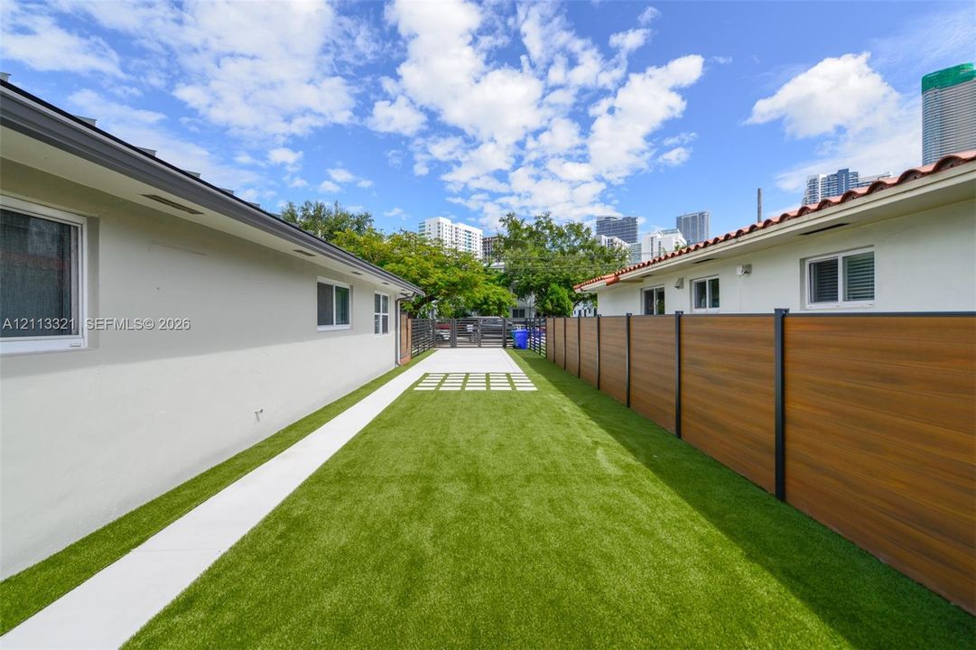 Exterior side yard featuring synthetic turf, concrete paver path, wood-finish privacy fencing, and metal gate
