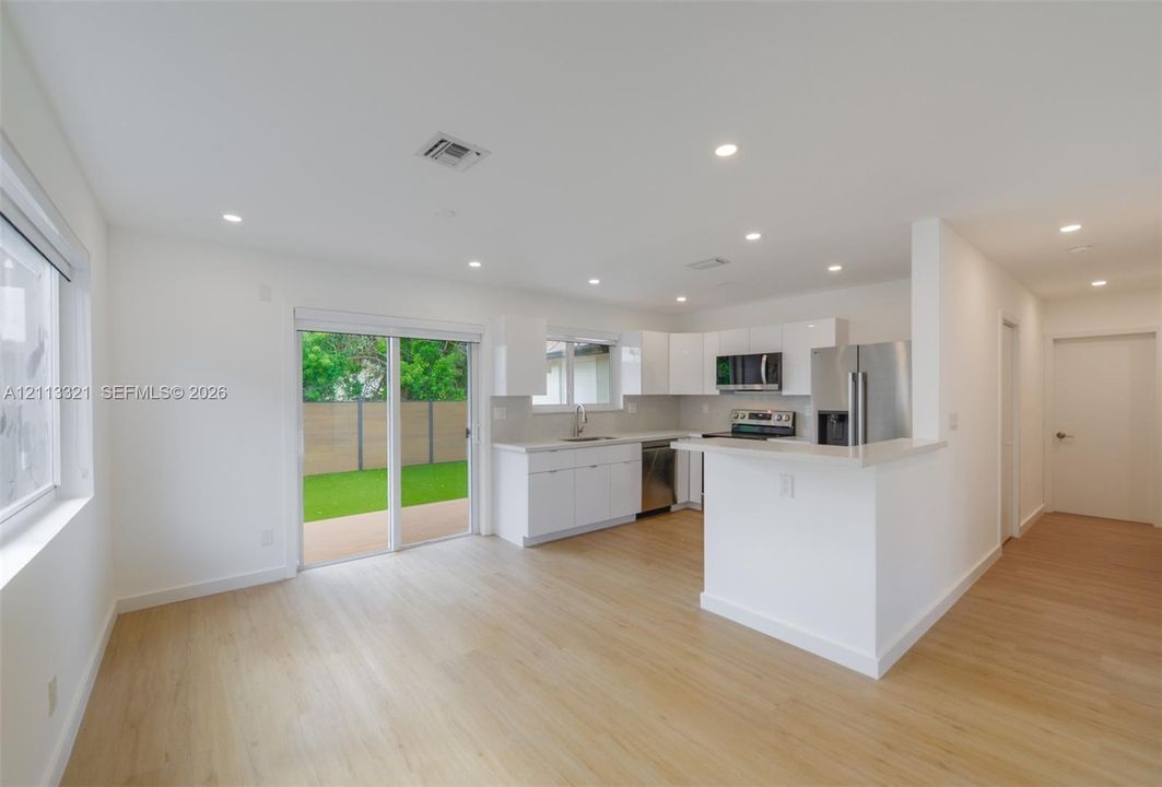 Kitchen featuring white flat-panel cabinetry, light-toned stone countertops, stainless steel appliances, recessed lighting, and wood-finish flooring