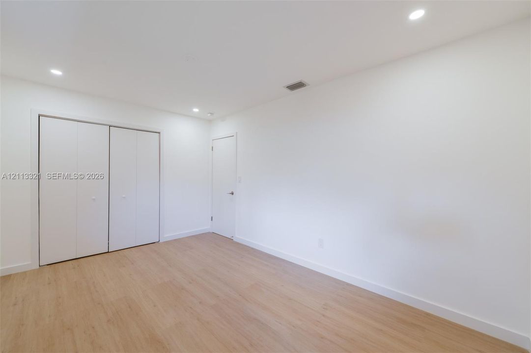 Neutral-toned wood-finish flooring, recessed lighting, and white dual-panel closet doors