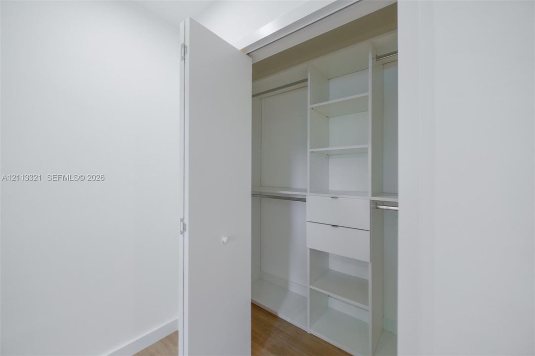 Custom closet featuring white built-in cabinetry, dual drawers, integrated shelving, and metal hanging rods over wood-finish flooring