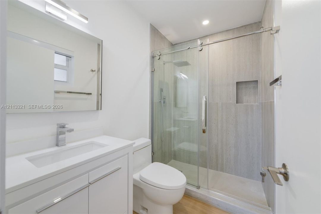 Bathroom featuring a white vanity with a countertop basin, a frameless glass shower enclosure with sliding doors, a recessed wall niche, and large-format tile shower surround