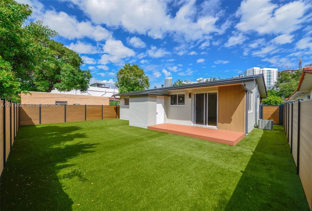 Backyard featuring a synthetic turf lawn, composite privacy fencing, raised deck, sliding glass doors, and vertical wood-slat siding