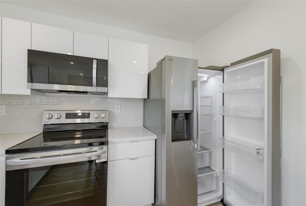 Kitchen featuring high-gloss white flat-panel cabinetry, stone-finish countertops, stainless steel microwave, stainless steel slide-in range, and stainless steel refrigerator with door-mounted ice and water dispenser