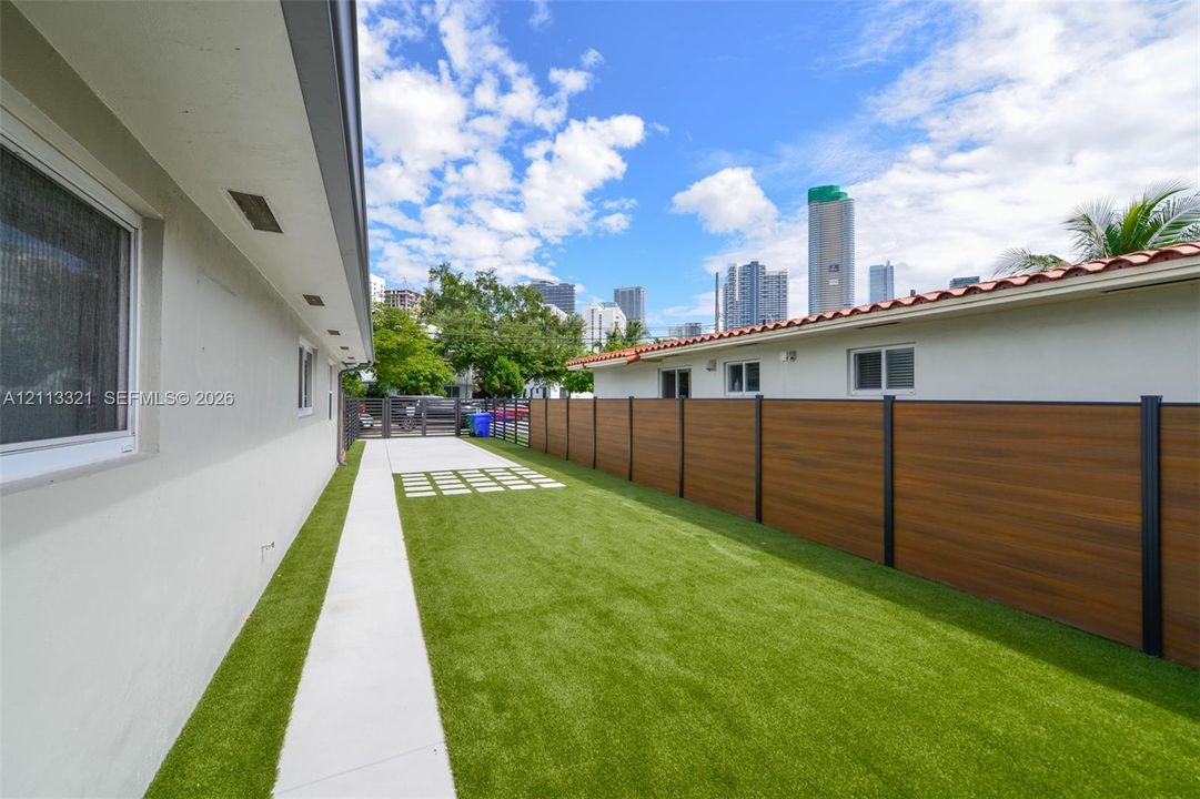 Side yard featuring synthetic turf, a concrete walkway, inset pavers, and a horizontal wood-composite privacy fence