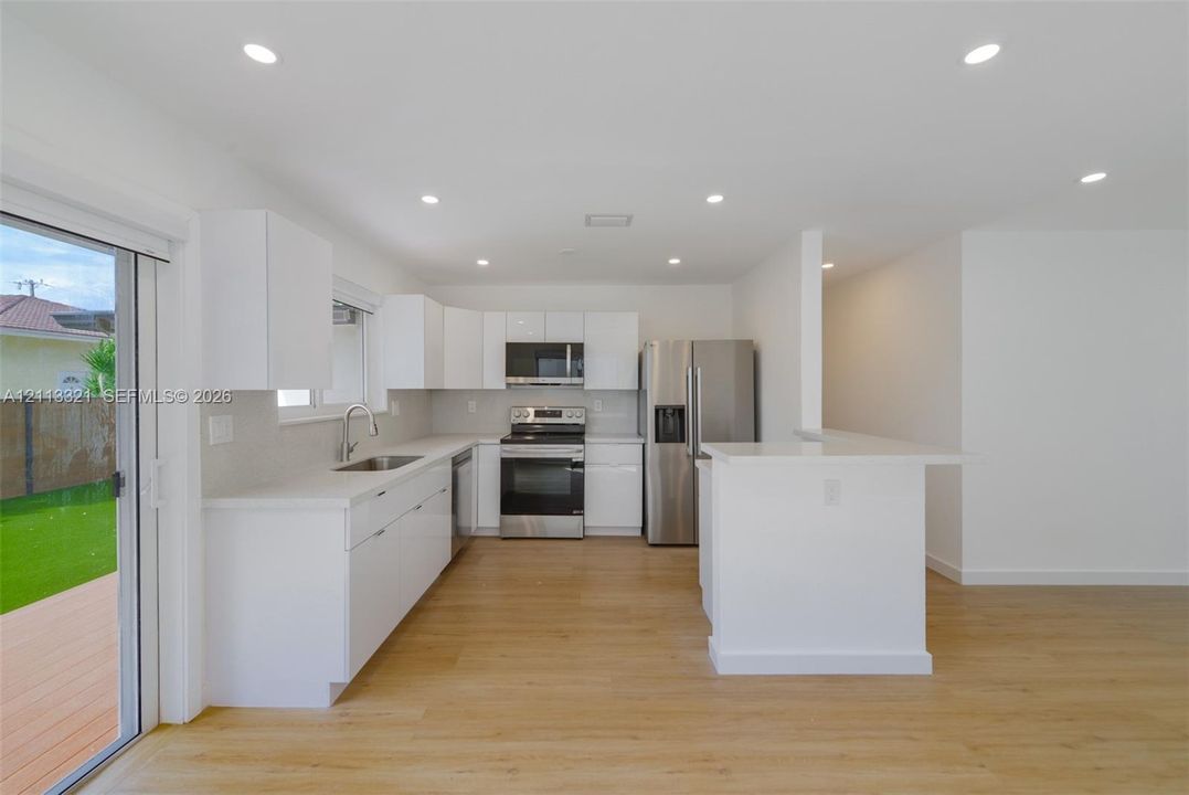 Kitchen featuring white cabinetry, solid-surface countertops, stainless steel appliances, wood-finish flooring, and recessed lighting
