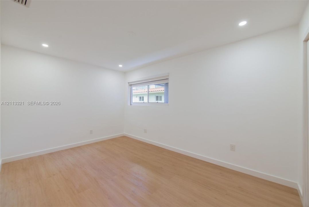 Neutral interior room featuring wood-finish flooring, recessed lighting, and a window with a horizontal blind