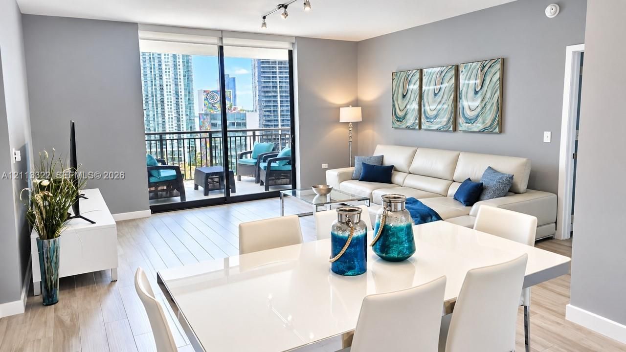 Open-concept interior featuring wood-finish flooring, floor-to-ceiling sliding glass doors, and a private balcony with an urban skyline backdrop