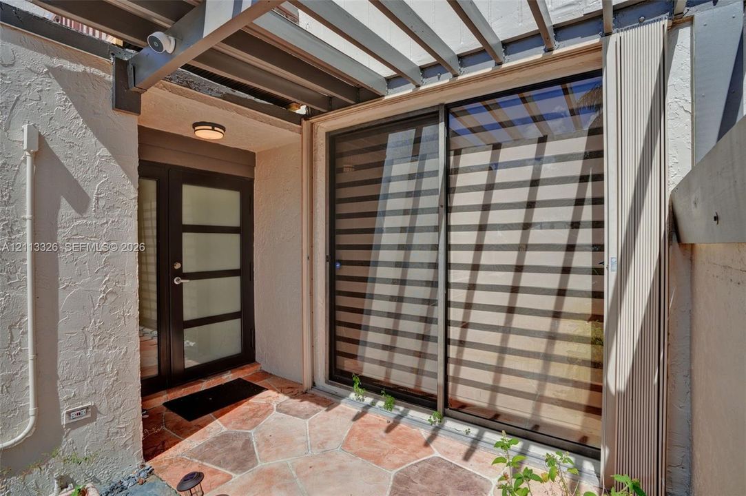 Patio featuring a structural pergola, stone-tile flooring, glass-paneled double entry door, and large sliding glass door