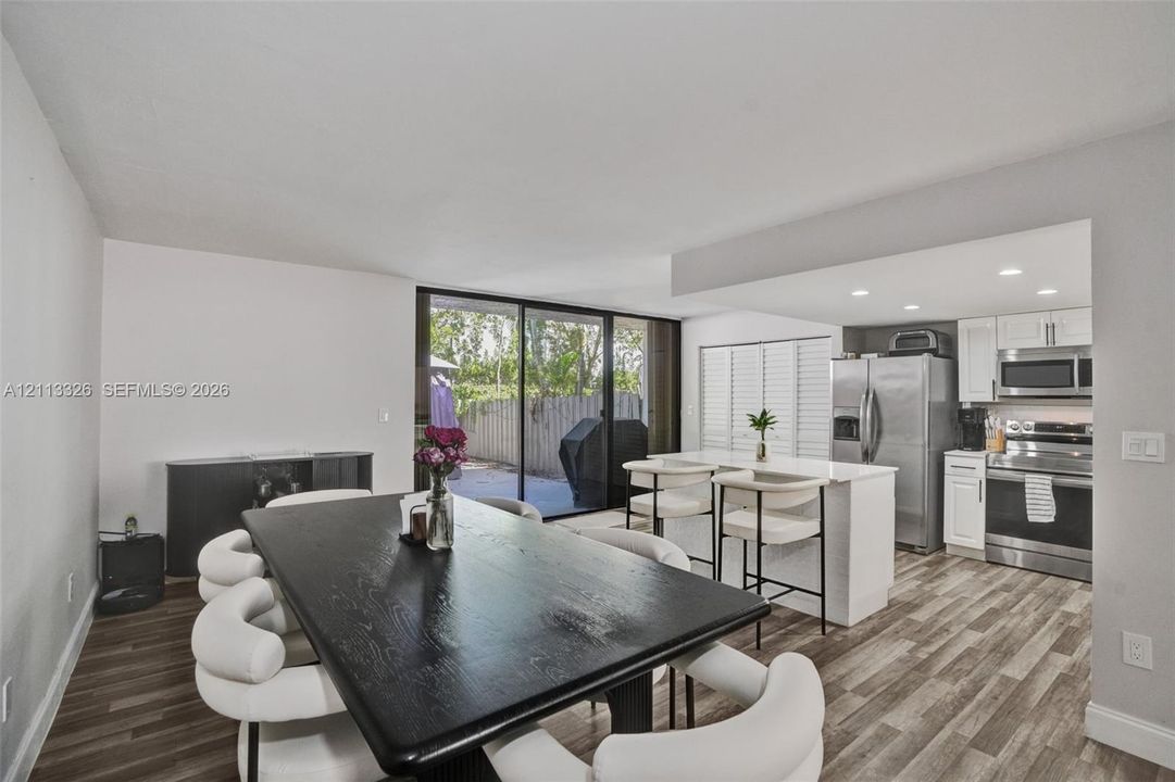 Open-concept interior featuring wood-finish flooring, kitchen island with stone countertop, stainless steel appliances, recessed lighting, and sliding glass doors
