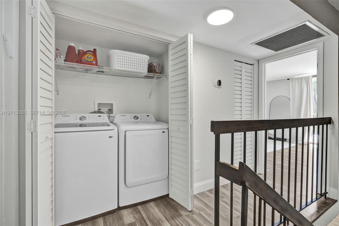 Laundry area featuring louvered bi-fold closet doors, integrated wire shelving, and wood-finish flooring, complemented by a dark-stained wood stair railing