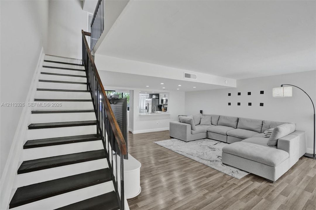 Staircase featuring dark wood treads and a metal handrail, wood-finish flooring, recessed lighting, and a kitchen pass-through window